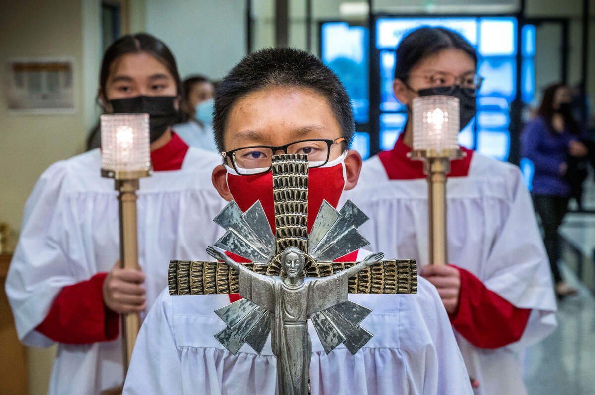Jóvenes miembros de la Parroquia de los Mártires Vietnamitas en el sur de Sacramento llevan una cruz y velas mientras caminan por el pasillo para celebrar el Jueves Santo.