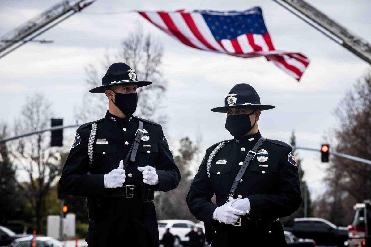 Members of the honor guard with the Orange Police stand in front of a flag that honors the memory of the fallen officer Deputy Adam Gibson at Bayside Church Adventure Campus in Rocklin on Wednesday, Feb. 3, 2021.