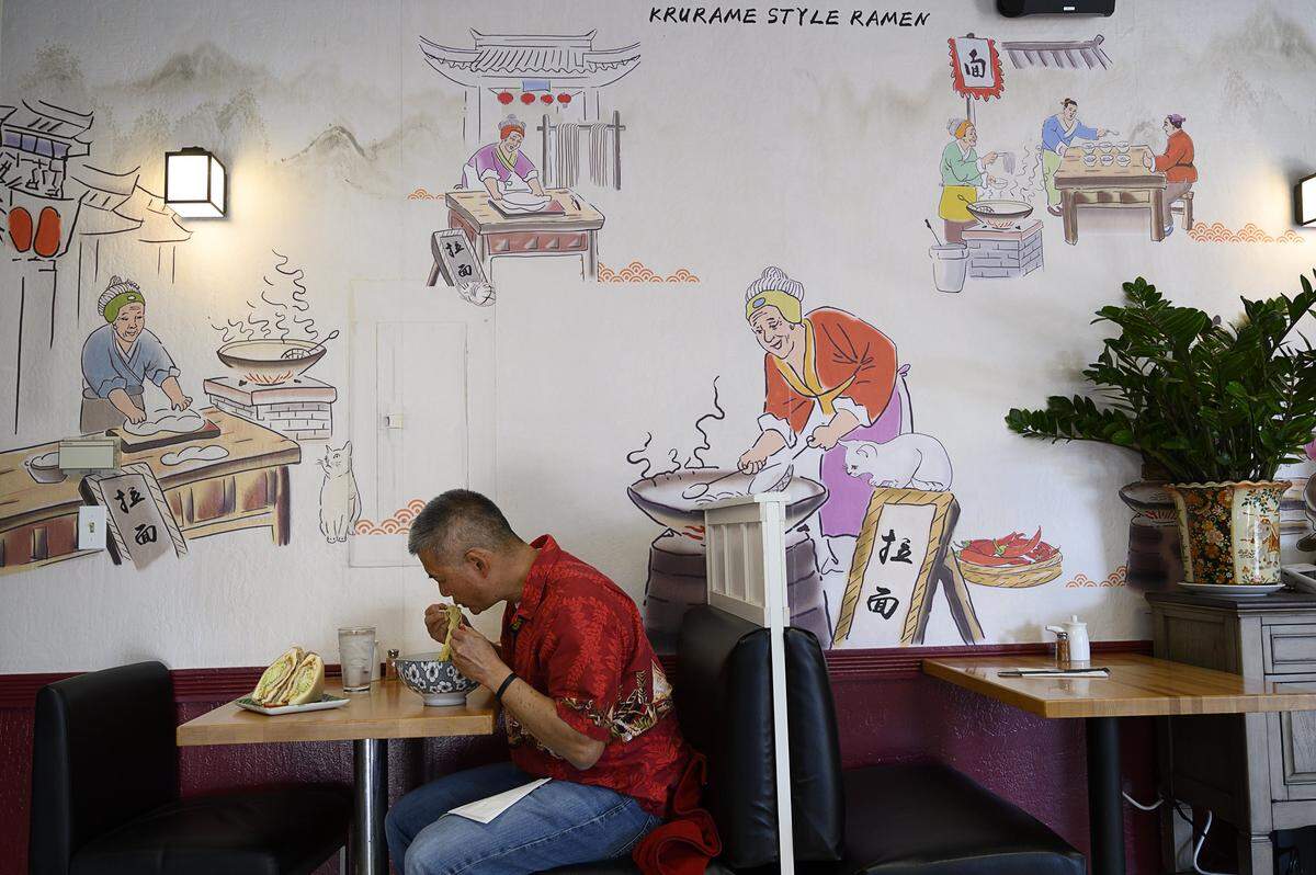 Bob Gong eats ramen at Shoku Ramen in East Sacramento on Friday, Nov. 15, 2019, under a line-drawn mural of people cooking noodles under the watchful eye of cats.