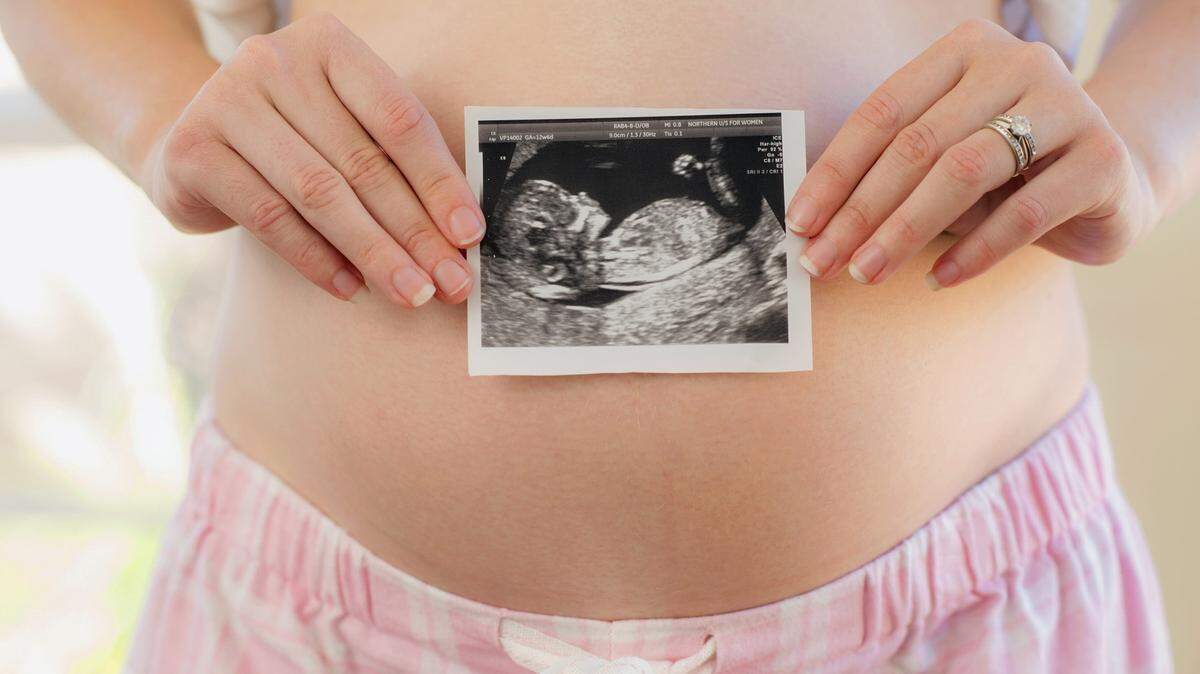 A woman holds a sonogram over her pregnant belly.