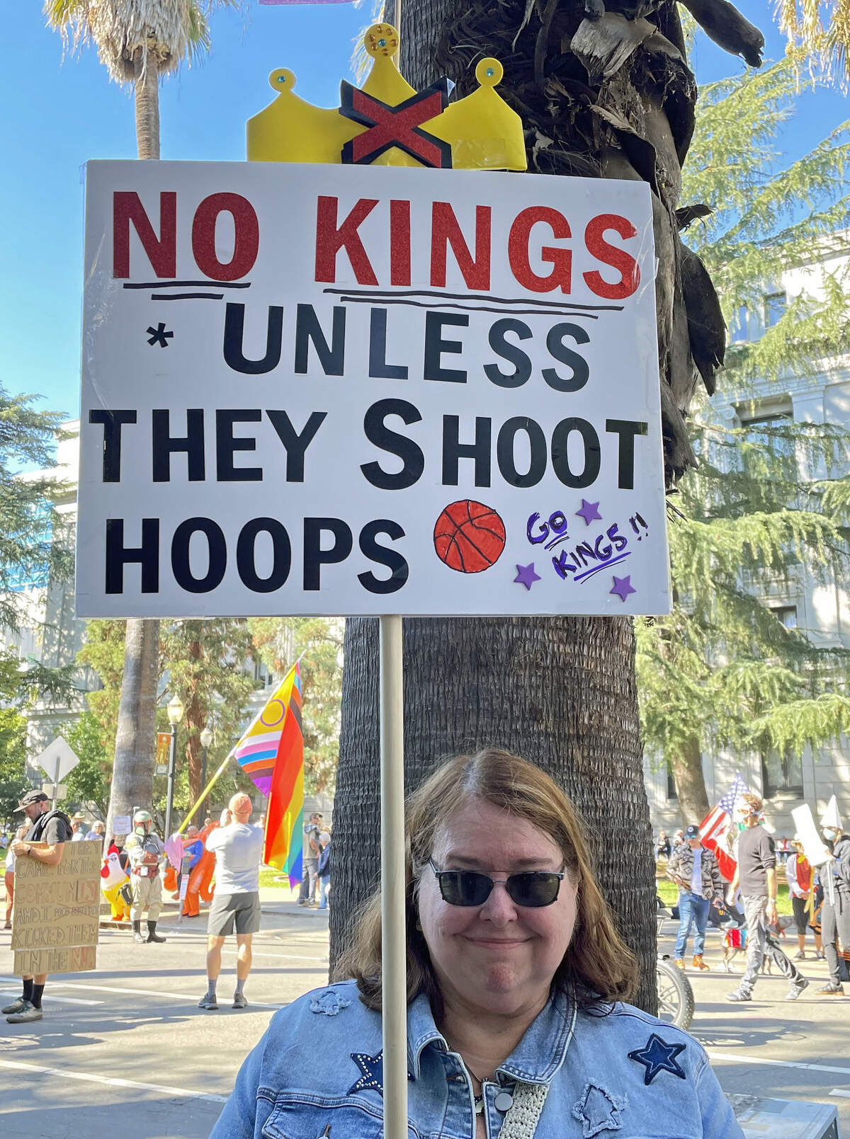 Debbie Sloan holds a sign at the “No Kings” rally on Oct. 18, 2025 at the Capitol touting the Kings she prefers.