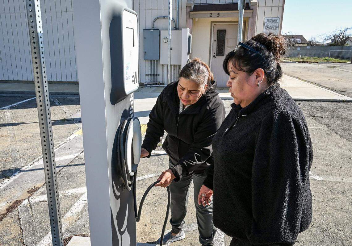 Fresno County residents Julia Mendoza, center, and Blanca Gomez re-wrap an EV charging station cable at an abandoned electric vehicle parking lot in the center of Cantua Creek in February. EV charging infrastructure is one of the areas where Gov. Gavin Newsom plans to make cuts to balance the state’s budget.