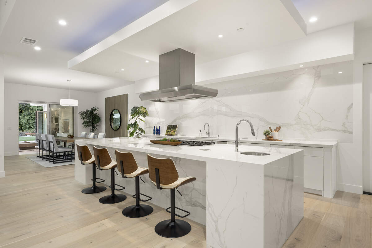 Stone and porcelain surfaces wrap the kitchen’s appliance wall and waterfall island, a bold, modern centerpiece designed to keep the open layout feeling sleek.