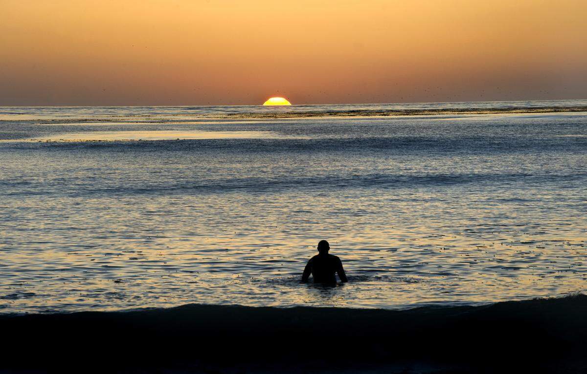A surfer watches the sun set from the ocean at Carmel-by-the-Sea in 2010.