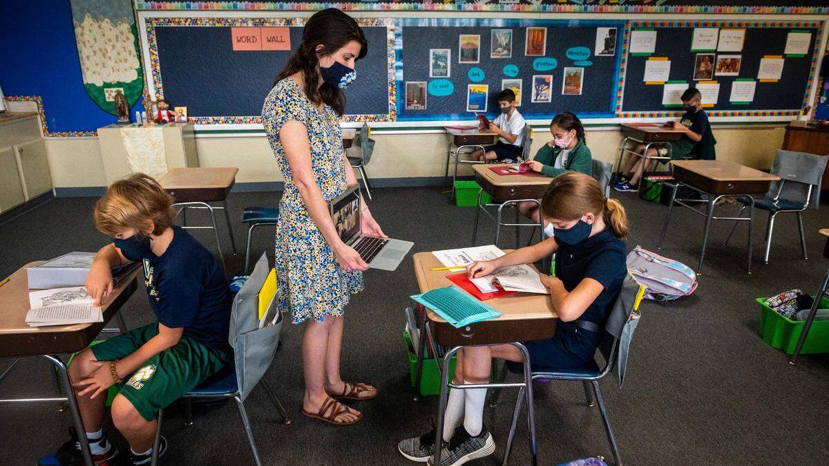 Fourth grade teacher Kalie Paranzino holds up a laptop as distance learning students on a video call listen to students in class read from a book during the first day of in-person instruction at St. John Vianney School in Rancho Cordova on Monday, Sept. 14, 2020. The school is one of 19 private schools – 16 run by the Catholic diocese – in Sacramento County granted waivers last week allowing in-person teaching during the coronavirus pandemic.
