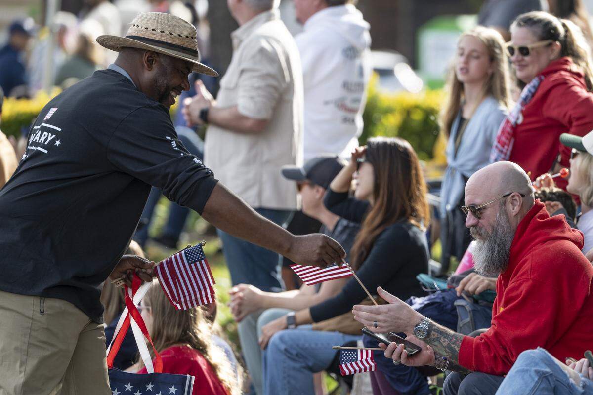De Vaughn Cross, left, passes out American flags during a Veterans Day parade in Folsom on Tuesday, Nov. 11, 2025.