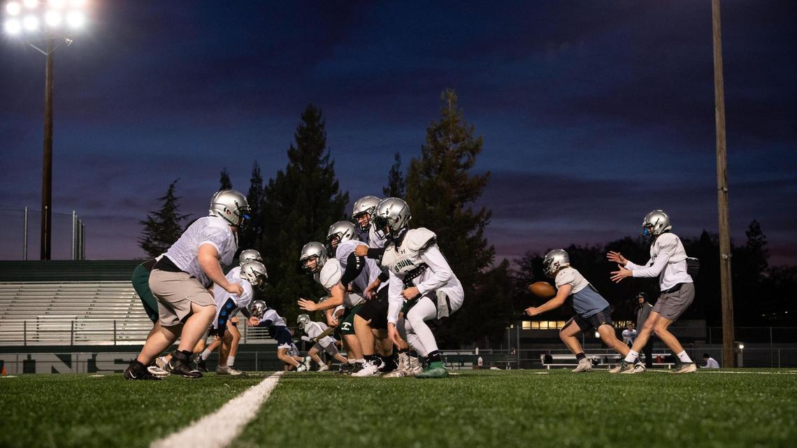 Ryan Hardt, far right, junior quarterback for the Ponderosa High School football team, takes a snap as senior running back Cody Pomi, at right near Hardt, moves into action during the team’s first padded practice back at the school Friday, Feb. 26, 2021, in Shingle Springs.