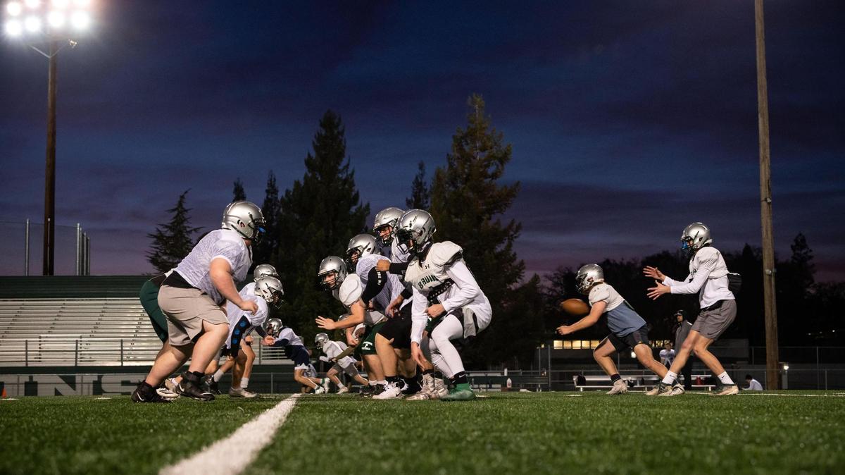Ryan Hardt, far right, junior quarterback for the Ponderosa High School football team, takes a snap as senior running back Cody Pomi, at right near Hardt, moves into action during the team’s first padded practice back at the school Friday, Feb. 26, 2021, in Shingle Springs.
