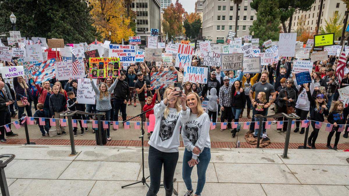 Tess Van Dusen y Amber Faddis, ambas con sudaderas de "mamá oso", se toman una foto el lunes 15 de noviembre de 2021, con una multitud de unas 1,000 personas que asistieron a una manifestación en el Capitolio del estado en Sacramento contra el mandato de vacunación para los niños en edad escolar. Van Dusen y Faddis también organizaron la concentración contra el mandato de vacunación el mes pasado.