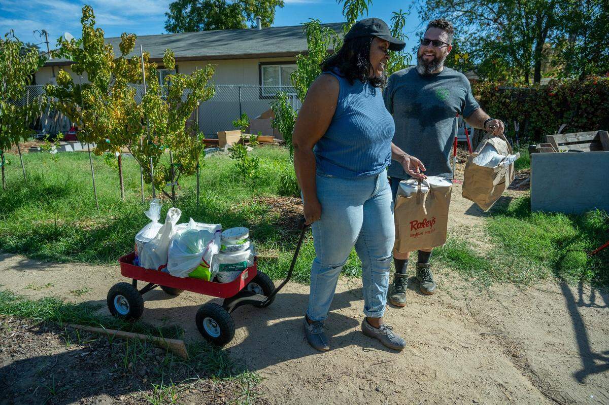 Robin Moore, 61, pulls groceries and supplies, delivered from a mission group from Fremont Presbyterian Church, earlier this month with help from Maximilian Rosa, director of sustainability of the Sierra Service Project, along the path of a community garden next to a Safe Harbor tiny home community she created. Moore partners with Family Promise to run the tiny home community, in her backyard in Del Paso Heights.