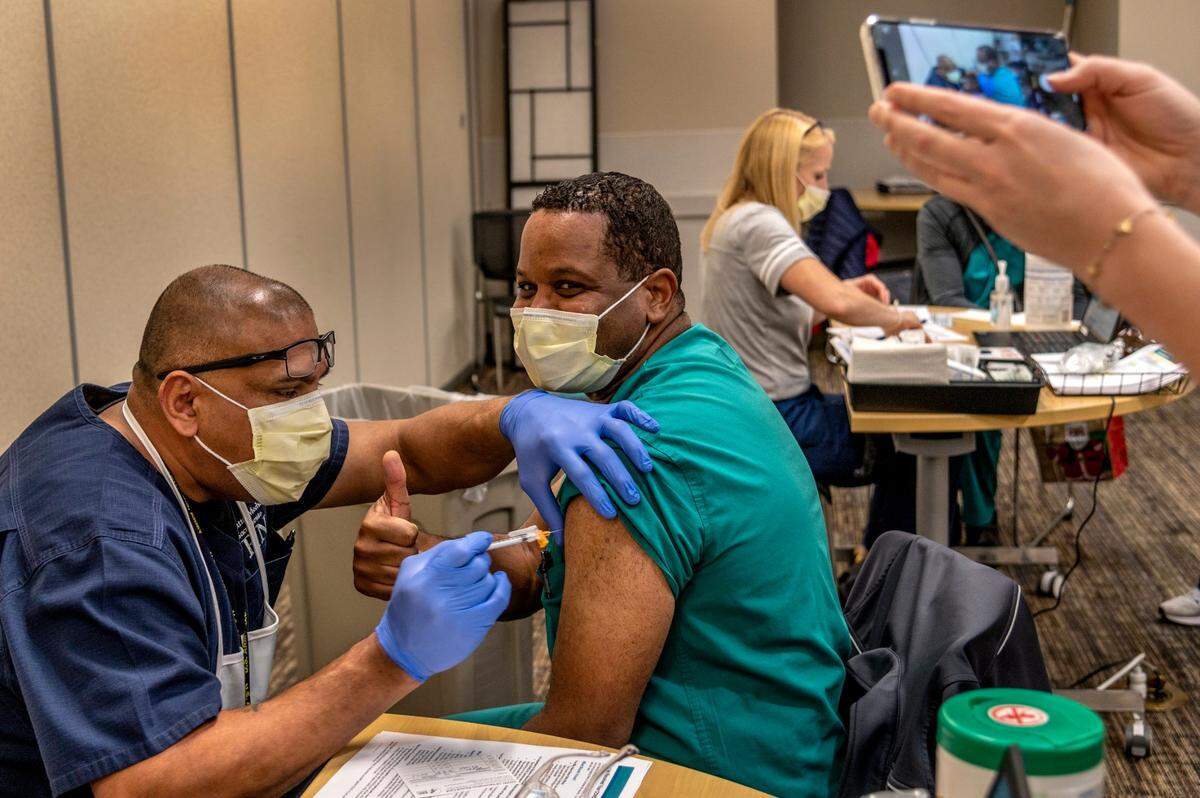 Nurse practitioner Robert McCary gives the thumbs up as his picture is taken while nurse Anil Shandil gives him the Pfizer-BioNTech COVID-19 vaccine shot at Sutter Medical Center, Sacramento on Friday, Dec. 18, 2020. They both served in the Army reserves together.
