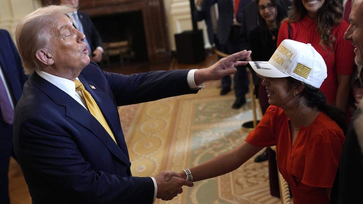 President Donald Trump greets a guest wearing a MAGA hat at a reception with Republican members of Congress in the East Room at the White House on Tuesday.