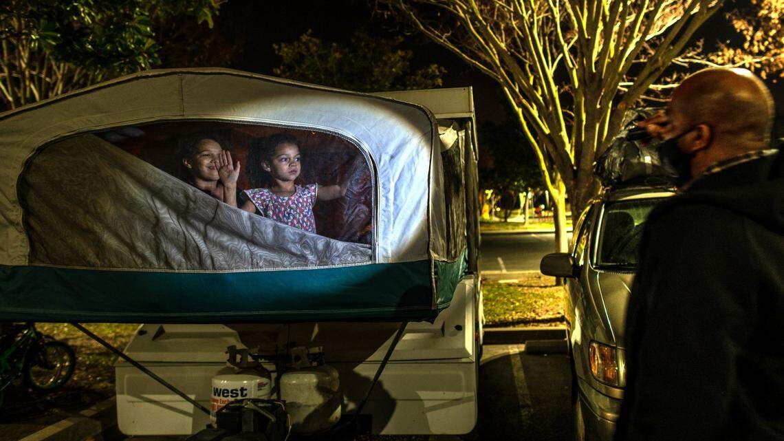 Aryanna Slain, 8, left, and Shyann Slain, 7, right, wave goodnight to their dad Anthony Slain, 45, before going to sleep in a camper after their parent’s couldn’t pay for another nights motel at South Natomas Community Park on Saturday, Jan.17, 2021. “As long as my kids are smiling I don’t feel too bad,” said Slain while shining a flashlight on them to make sure they are zipped in okay.