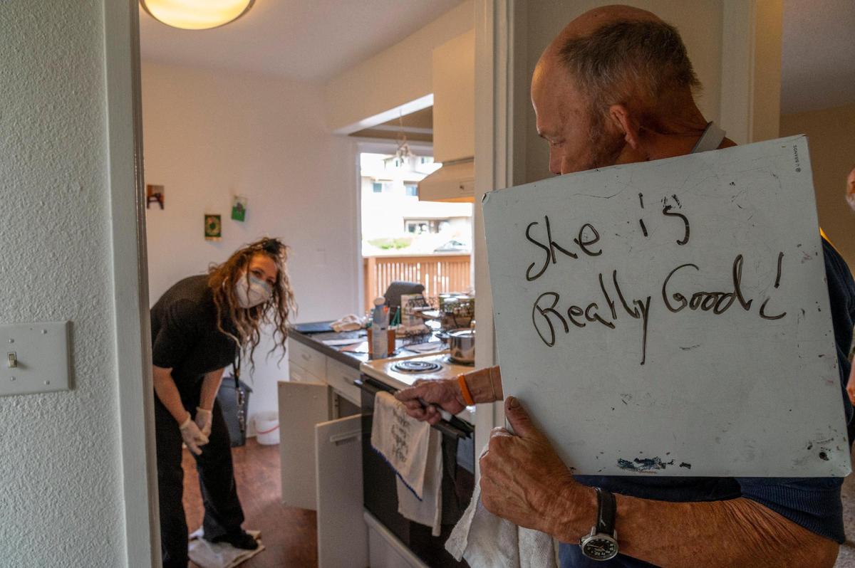 Jim Wilson, holds a message board with his thoughts about his palliative care nurse Denise O’Donoghue, as she looks over his food in his cabinets to figure out a better diet for him on Friday June 12, 2020.