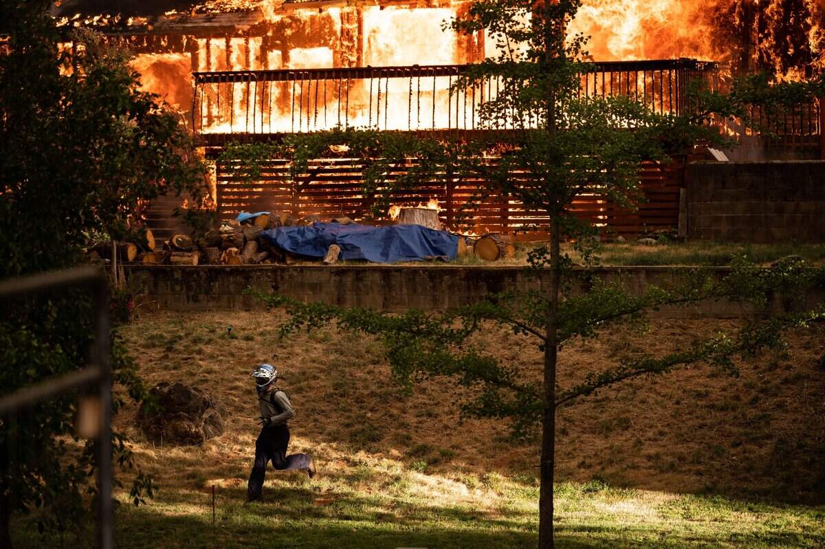 A man quickly leaves after checking the situation of a fully involved house burning on the 16000 block of Mount Olive Road during the River Fire on Wednesday, Aug. 4, 2021, in Nevada County.