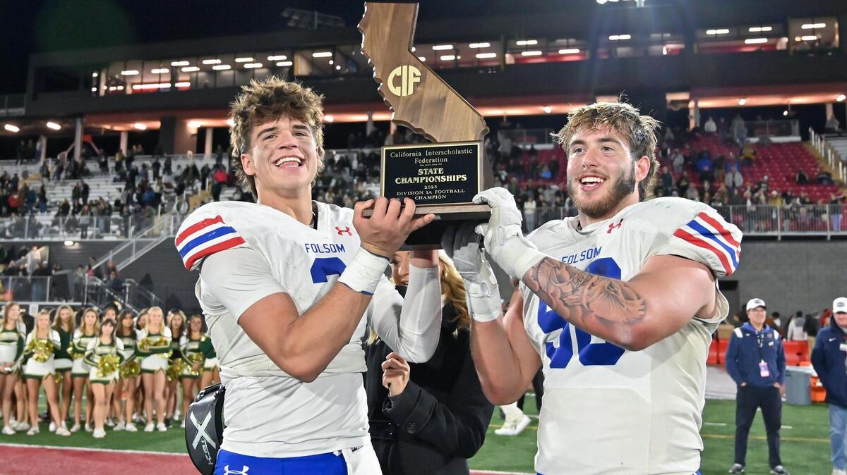 Folsom Bulldogs quarterback Ryder Lyons (3) and defensive tackle Lucas Hardeman (56) hold the state championship plaque on the podium after winning the CIF division 1-A state football championship against the St. Bonaventure Seraphs on Saturday, Dec. 9, 2023, at Saddleback College in Mission Viejo.