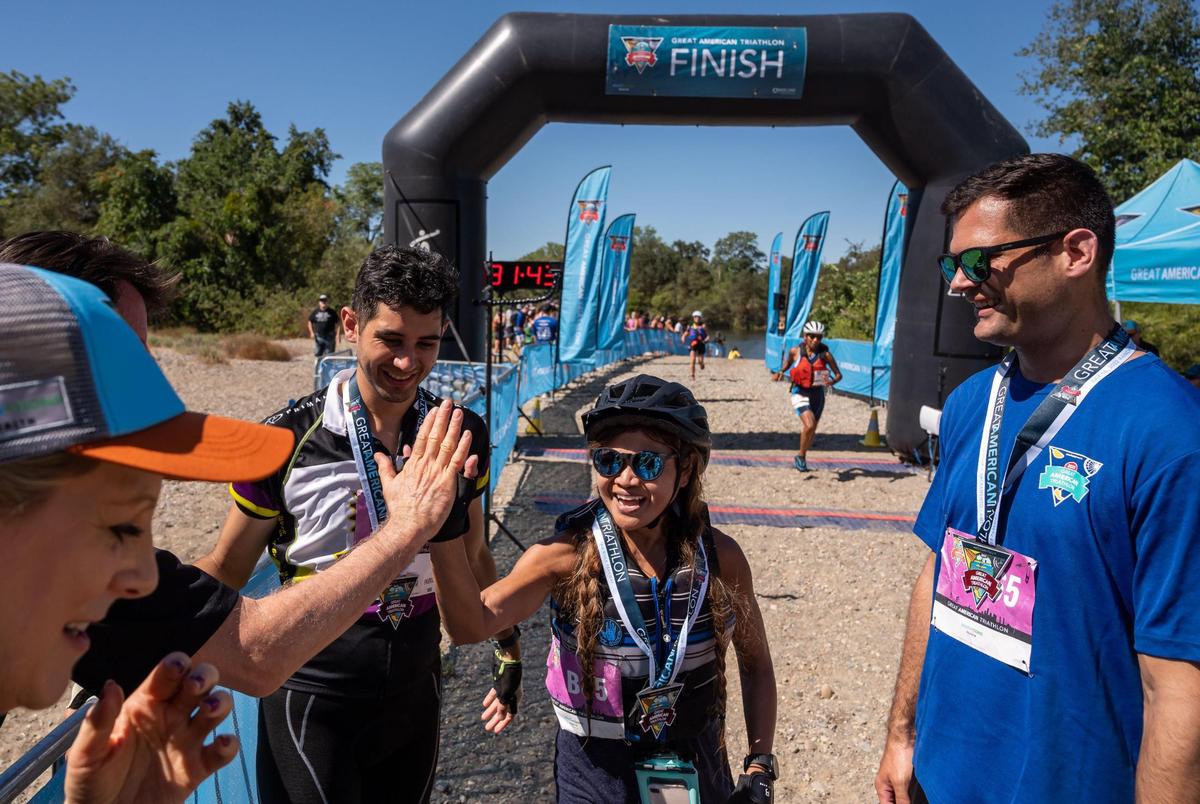 Michelle Carrasco, center, is congratulated by supporters while flanked by teammates Matthew Valenzuela, left, and Zach Gonzalez after completing the paddle portion of the Great American Triathlon, previously known as Eppie’s Great Race, on Saturday at River Bend Park in Rancho Cordova. “We all run with Elk Grove Fleet Feet,” Carrasco said, adding that they connected for the first time two weeks ago to form Team RACE — Random Athletes Connect Eventually. “We did really well today, I’m so proud of us!”