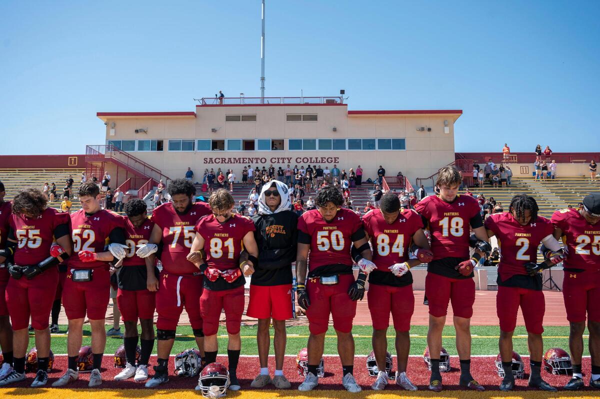 Members of the Sacramento City College football team lock arms to stand for a moment of silence in honor of 19-year-old offensive tackle Justin McAllister prior their game on Saturday, Sept. 16, 2023, at Huges Stadium. McAllister died during a practice Sept. 11.