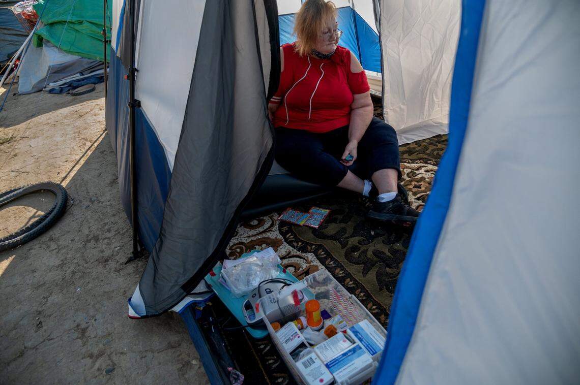 After a long walk to her tent at the Morrison Creek encampment, Betty Rios, 48, sits exhausted, clutching her inhaler. She suffers from asthma and worries how she will use her electric breathing machine now that she had to leave her Project Roomkey housing.