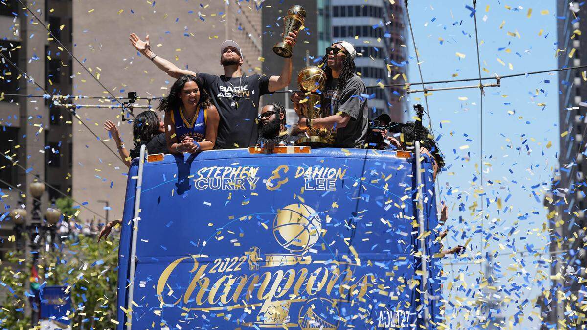 Golden State Warriors guard Stephen Curry holds his MVP trophy as guard Damion Lee holds the championship trophy during the Warriors championship parade in downtown San Francisco in 2022.