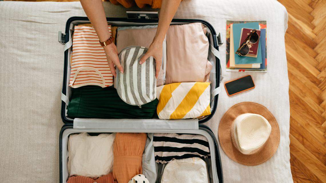 Shot from above of an anonymous woman packing things in her suitcase on the bed. 