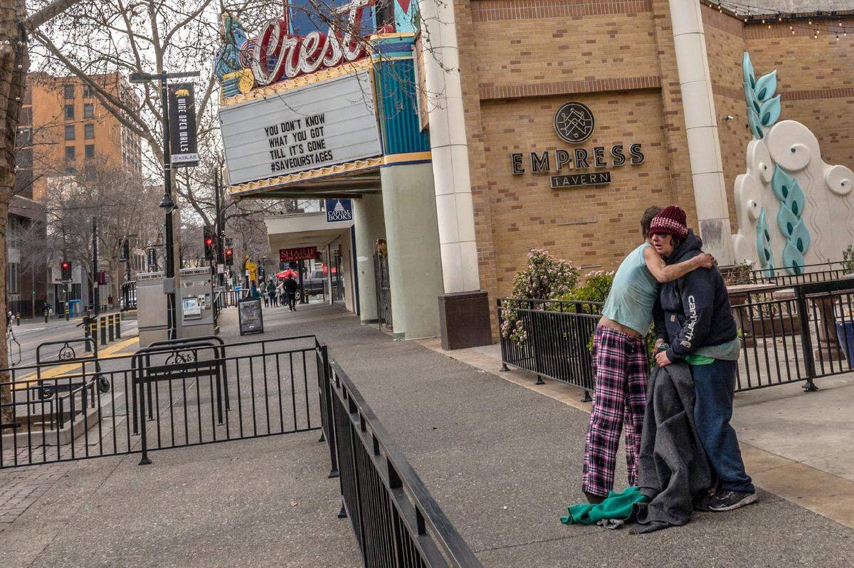 A homeless women embraces another who suffered a blackened eye, as they stand near the closed Crest Theater in downtown Sacramento on Feb. 18, 2021, with a marquee that reads, “you don’t know what you got until it’s gone.”