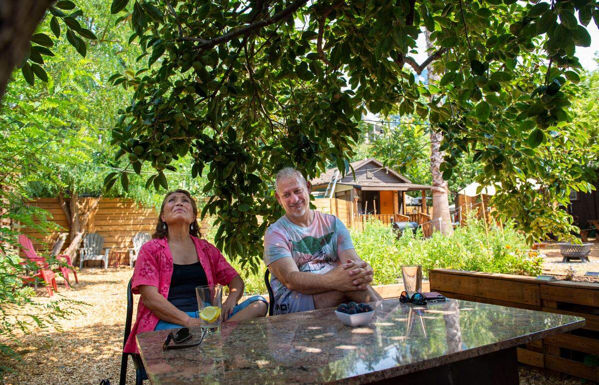 Monica Guillen, left, looks up at the trees her father planted while sitting with Restaurantuer Jeff Davis at Tree House Cafe in West Sacramento on Wednesday, Aug. 11, 2021. Guillen grew up in the home that is now the cafe. The fruit from the trees are used in the dishes they offer.