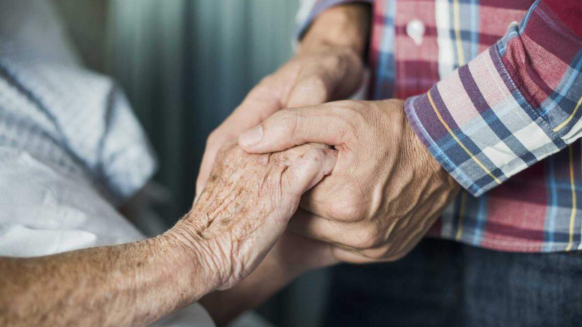 A stock image of people holding hands in a hospice care setting.