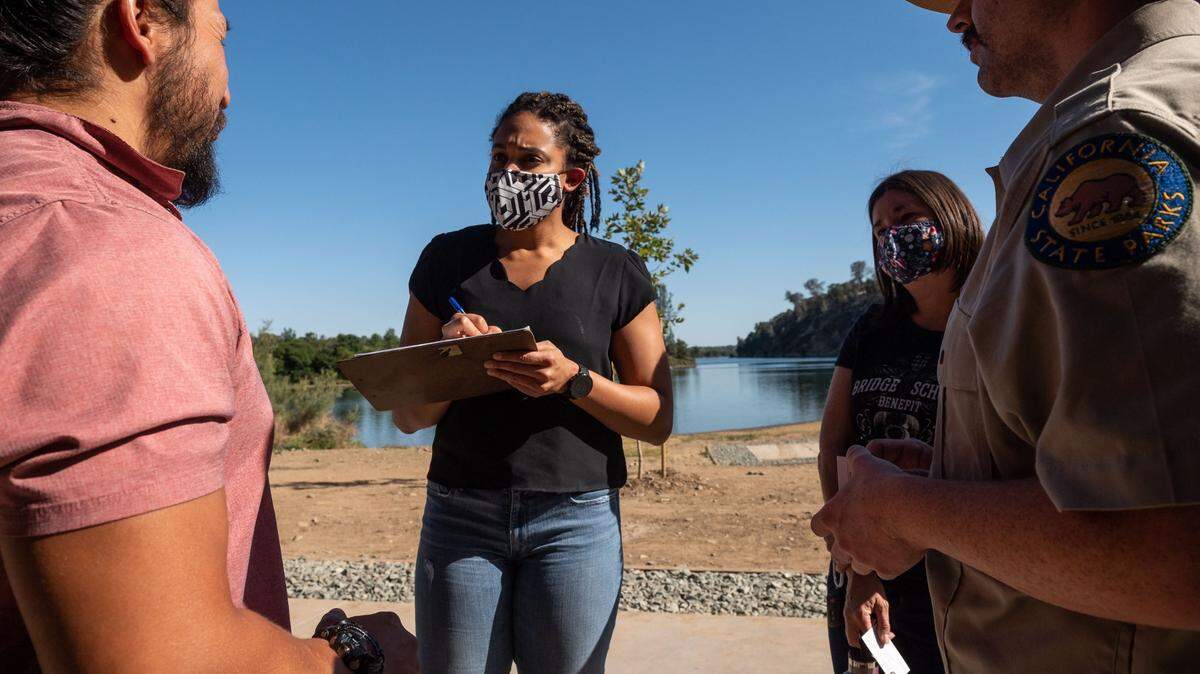 Jenn Johnson, with Conscious Cultural Connections, gathers information from Travis Young, a United Auburn Indian Community member of Nisenan descent, next to California State Parks interpreter Devin Swartwood at Negro Bar in the Folsom Lake State Recreation Area on Thursday, June 10, 2021, after a meeting to discuss the renaming of the historic park between stakeholders, community members and park officials. The site on the American River is where Black miners were the first to prospect during the Gold Rush, but the surrounding town of Folsom has developed into an area where few Black people live, Johnson said.