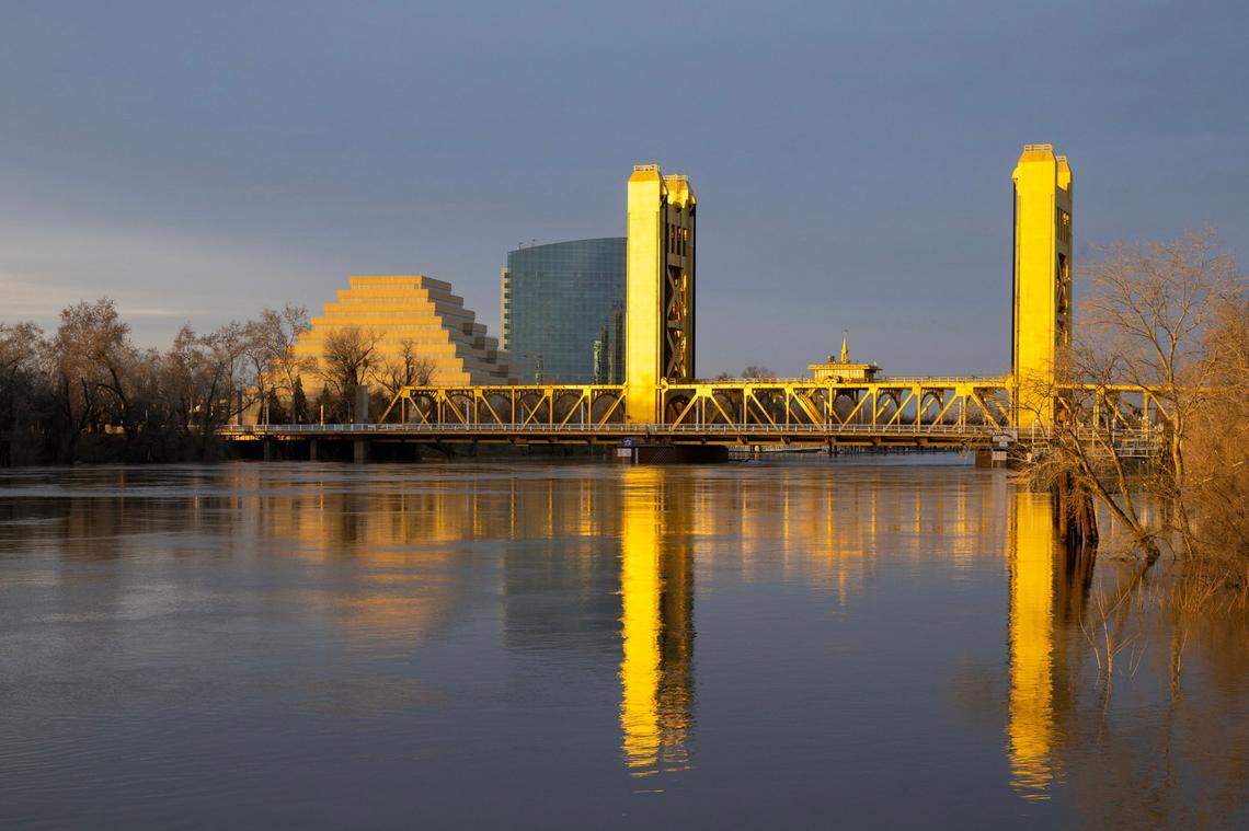 The Sacramento River, swollen from recent storms, flows under the Tower Bridge as the setting sun reflects off its golden paint on Monday. A nearby gauge indicated the river was a 27.7 feet, still below monitor stage.