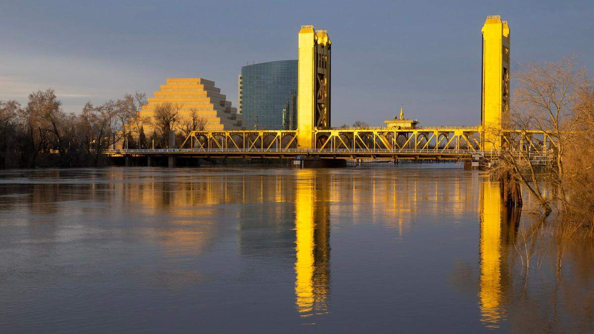 The Sacramento River, swollen from recent storms, flows under the Tower Bridge as the setting sun reflects off its golden paint on Monday, Jan. 9, 2023.