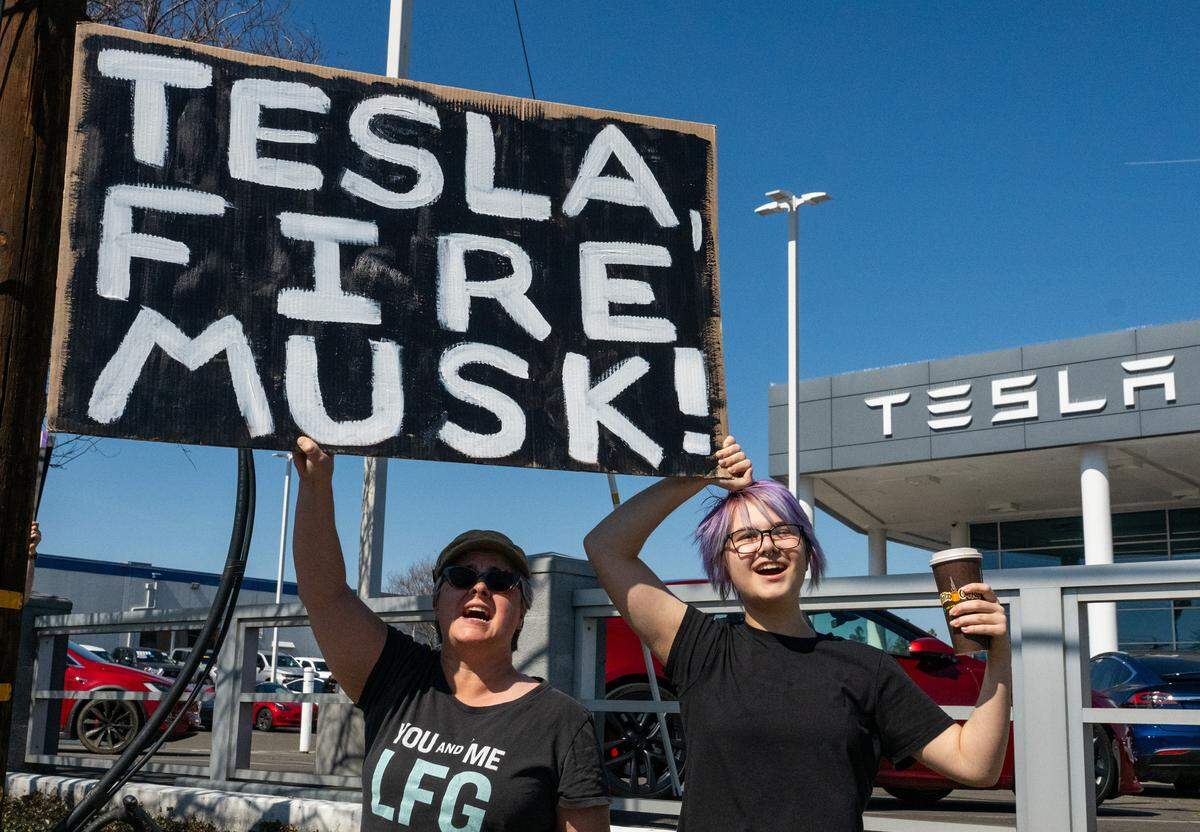 Sacramento residents Lori Gregg and daughter Max Pollitt, 16, hold a sign at a rally against Elon Musk at a Tesla dealership on Arden Way near Sacramento on Saturday, March 8, 2025. More than 100 people lined both sides of street to protest the role of the tech billionaire and Tesla CEO in the Trump administration.