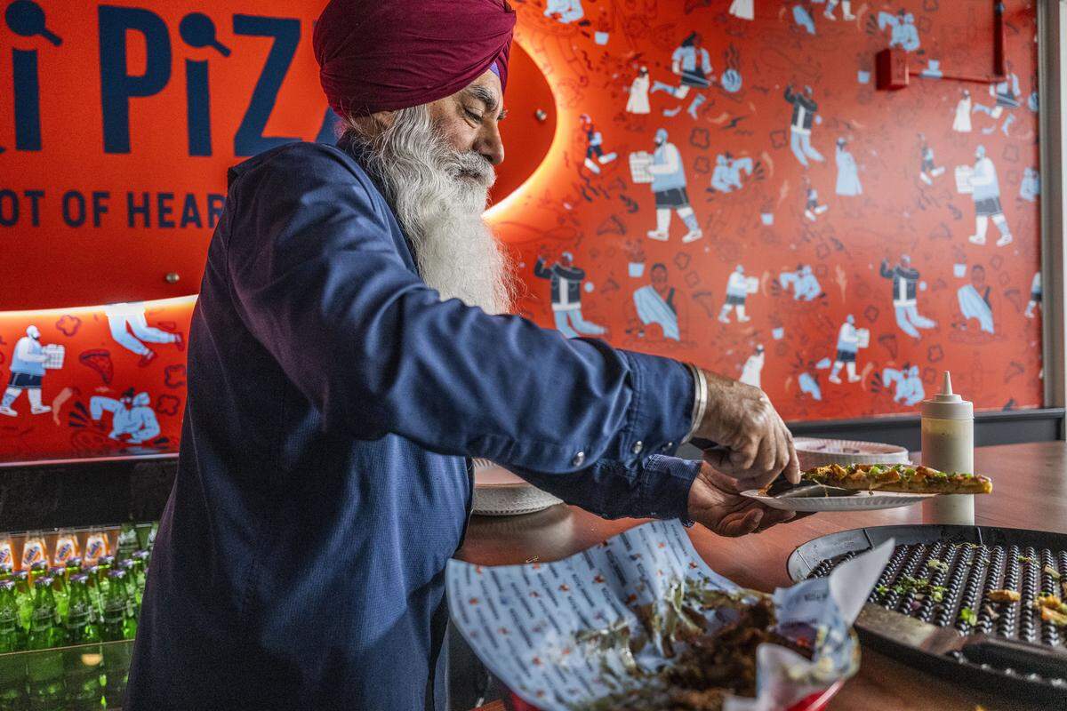 Paul Singh, the father of one of the owners of Tandoori Pizza at Downtown Commons, serves pizza Wednesday to guests during the restaurant's grand opening. 