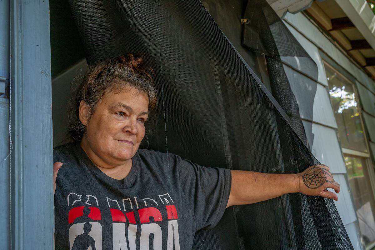 Tammy Myler, 57, pushes back a makeshift curtain she hung in her front door of her home in Sacramento to keep flies out and allow ventilation, since her windows don’t open and there is no screen door, in October. The former Camp Resolution resident said she applied for a housing voucher while living at the Railroad Shelter and credits Camp Resolution for giving her stability and a safe place to search for housing. She wishes she still lived there.