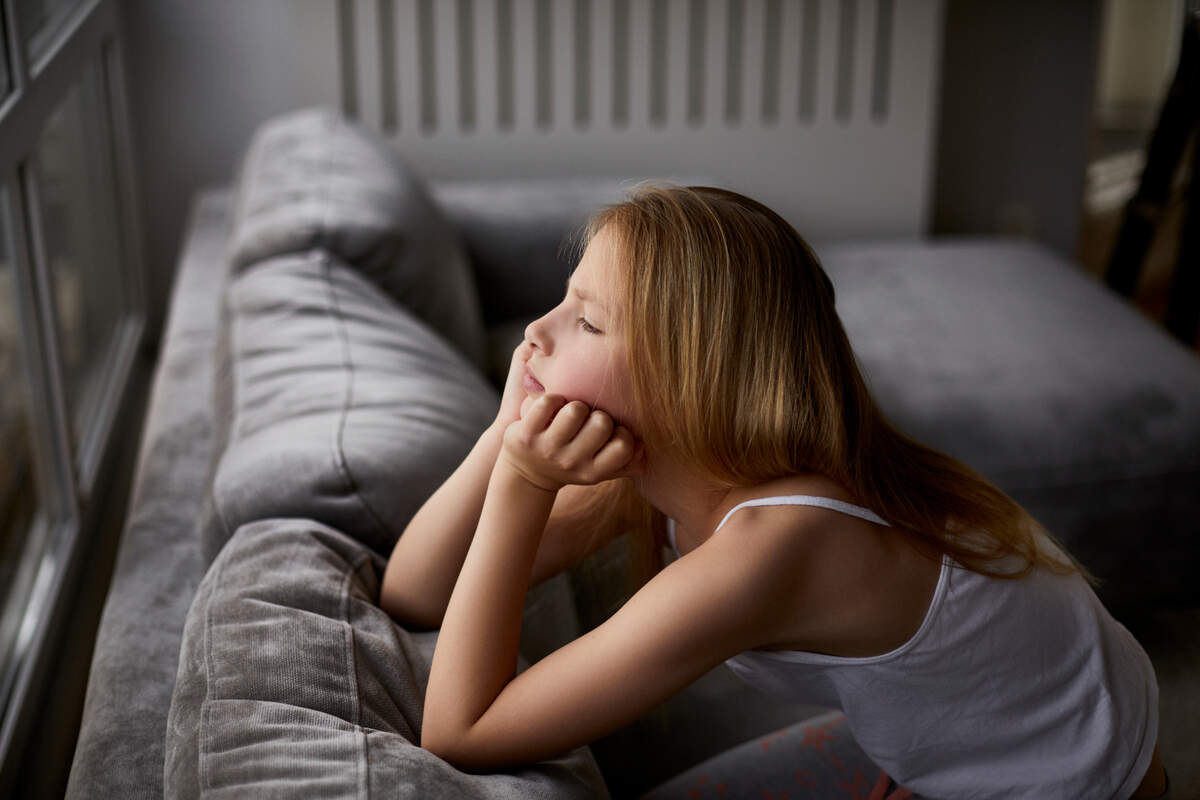 A girl looks out of the window after being left at home alone.