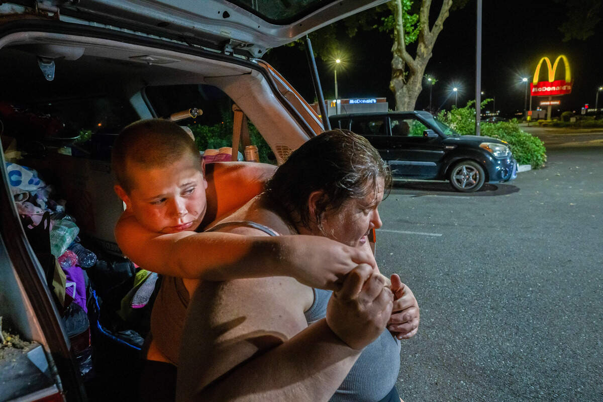 Unable to get comfortable sleeping in the back of their van, Amy Heckart, 46, and her son, Keith-Dalton Smith, 11, look out at other residents sleeping in their vehicles in a Taco Bell parking lot in Sacramento on Thursday. Heckart had been locked out of the Motel 6 after changes to a city-funded program.