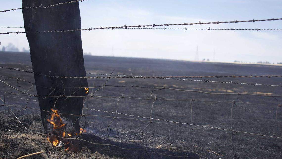 A fence smolders after a fast-moving grass fire burned Sunday, June 16, 2024, in an area of southeast Sacramento County. The Excelsior Fire burned more than 800 acres and destroyed at least two outbuildings along Jackson Road.