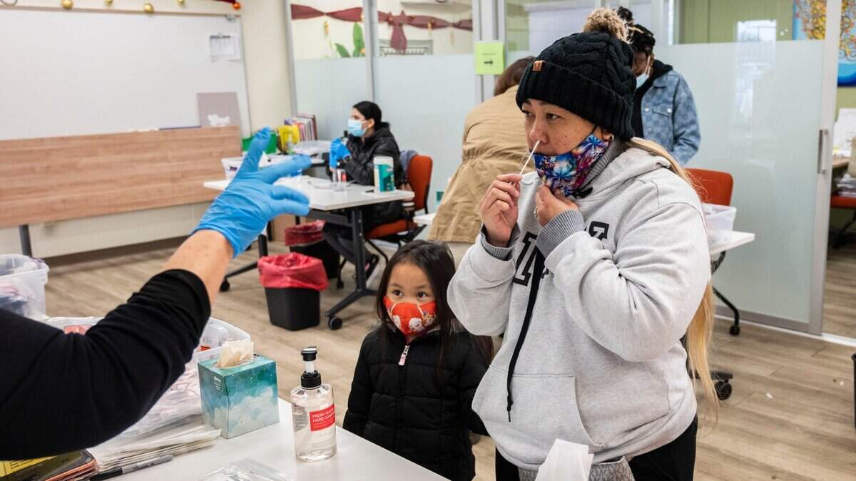 Mai Vang, de Sacramento, se somete a la prueba COVID-19 el lunes 3 de enero de 2022 en La Familia Counseling Center, en el sur de Sacramento, mientras su hija Ella Yang, de cinco años años, espera su prueba. Algunas personas esperaron más de dos horas en fila.