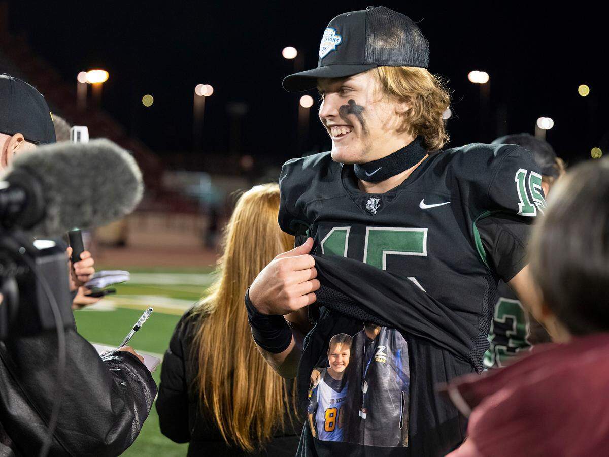 Twelve Bridges Raging Rhinos quarterback Connor Flaherty (15) pulls up his jersey on Friday, Nov. 29, 2024, to show members of the media the T-shirt he wears in remembrance of his stepfather Eric Morales, who died in 2017. Flaherty’s team scored 55 points against the Patterson Tigers to win the Sac-Joaquin Section Division IV championship game at Hughes Stadium.