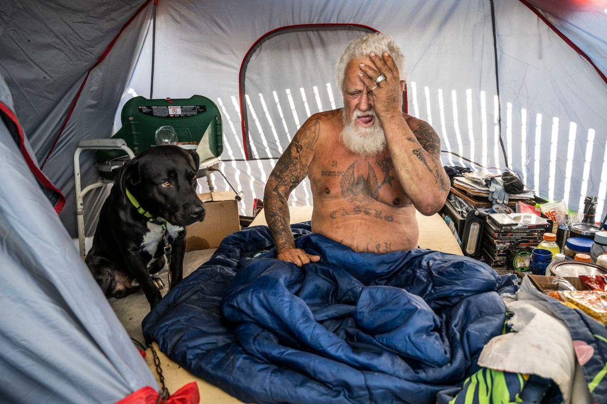 Mark Yates 70, who recently suffered a stroke sits, in his tent with his dog Brutus at a homeless encampment at Colfax Street on Wednesday, Nov. 2, 2022. The camp is on city property that state officials have deemed too toxic for people to inhabit. Like other campers at the site, he has received a city notice to leave the area. “I’m not gonna die out here,” said Yates, who refuses to believe that the site is toxic. He said he’s been homeless for two years.