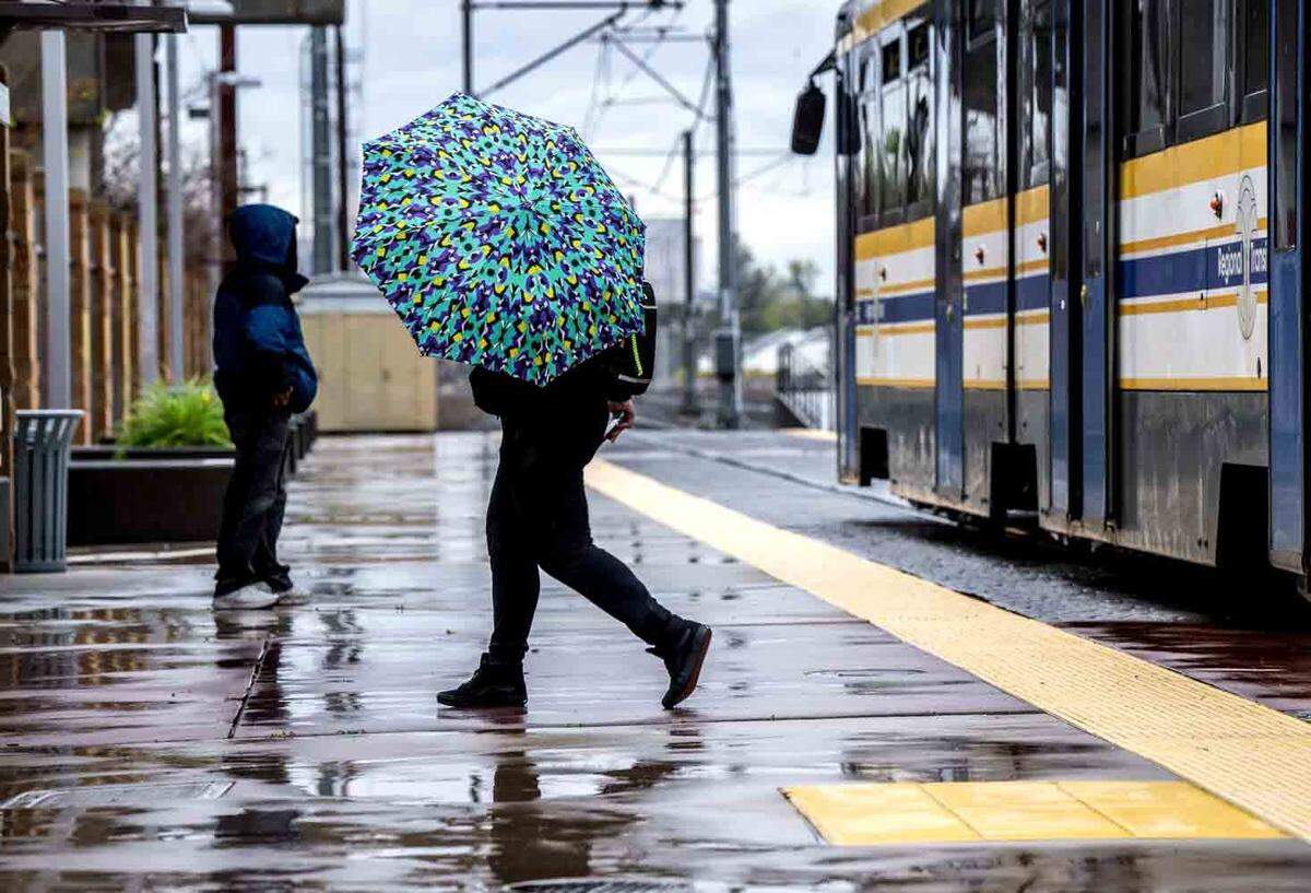 A light rail passenger departs the train with an umbrella at Sacramento City College in March 2023.