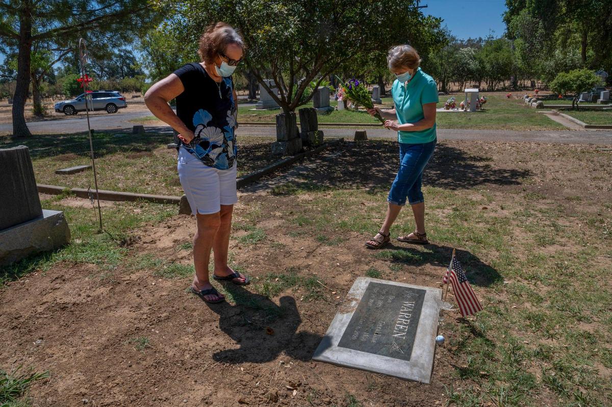 Donna Scully, left, and her sister Patti Warren visit their parents’ grave at the Capay Cemetery in Esparto on Thursday, July 9, 2020. Their parents, Don and Geraldine “Gerry” Warren, both died earlier this year at age 89 at the Stollwood Convalescent Hospital Skin Woodland. Gerry died on March 8 from complications of Alzheimer’s disease and Don died on April 16 from COVID-19 complications. “Bye mom, bye dad,” said Scully after giving a virtual hug to her sister as they left the cemetery.