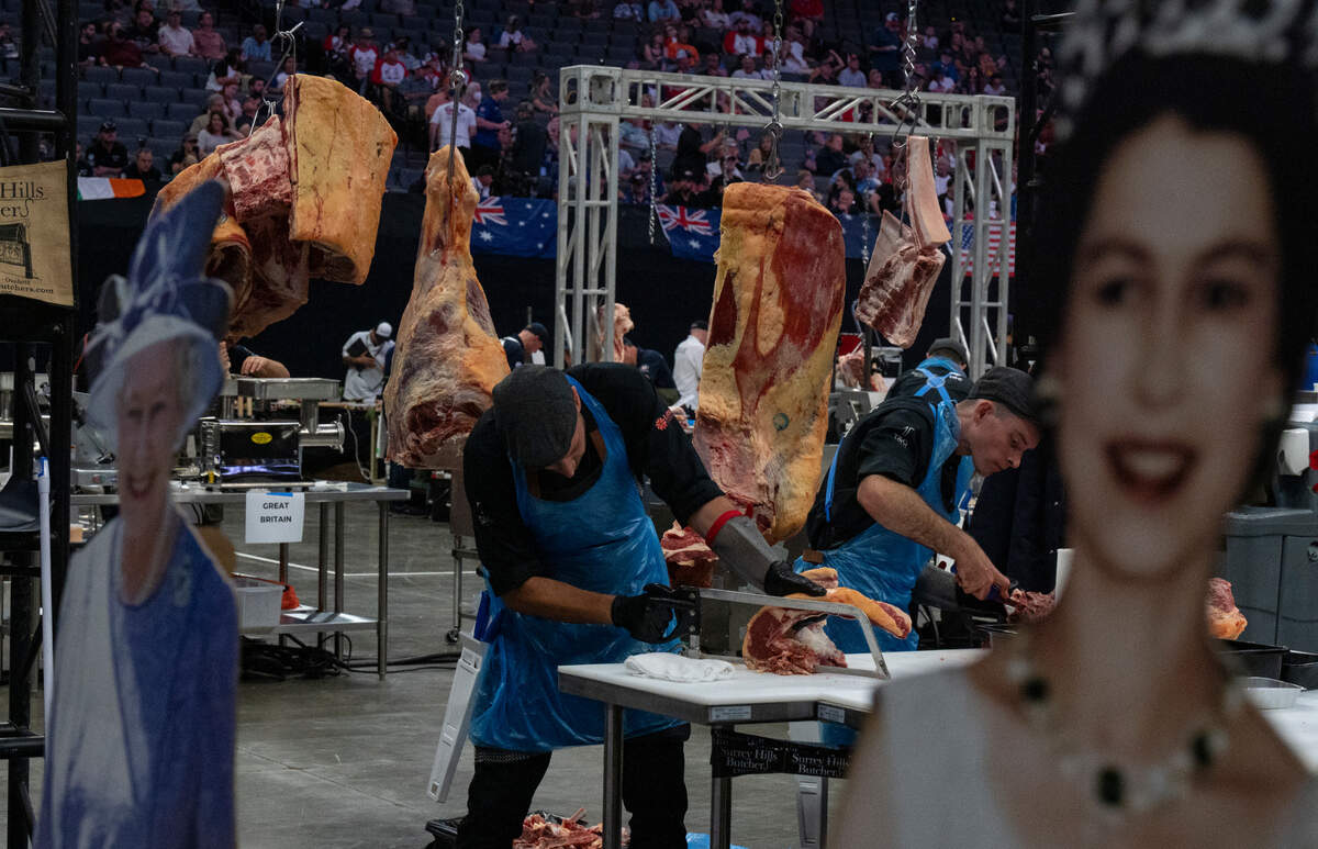 Framed by cutout portraits of Queen Elizabeth II, two member so Great Britian’s team cut up meat during the World Butchers’ Challenge at Golden 1 Center in Sacramento on Saturday, Sept. 3, 2022.