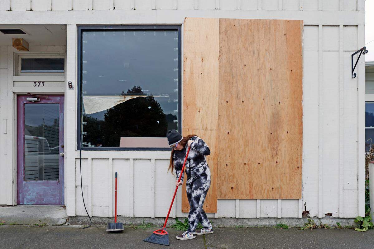 A person, who identified themselves as Michelle, sweeps the street from broken glass following an earthquake in Rio Dell, Calif., Tuesday, Dec. 20, 2022. (Santiago Mejia /San Francisco Chronicle via AP)