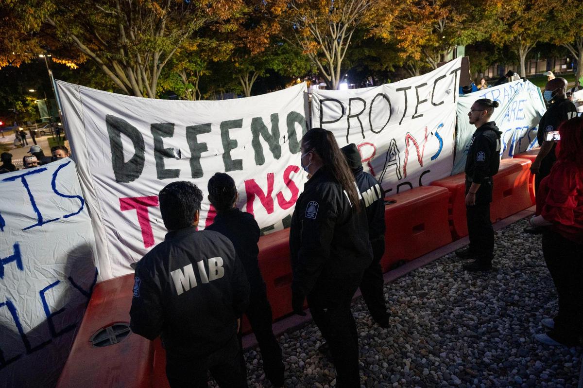 Protesters defending trans youth hold signs against a barricade protected by security outside the conference centers at UC Davis as speaker Riley Gaines, known for her outspoken views against&nbsp;trans-women in sports, prepares to speak Friday during her Speak Louder Campus Tour.