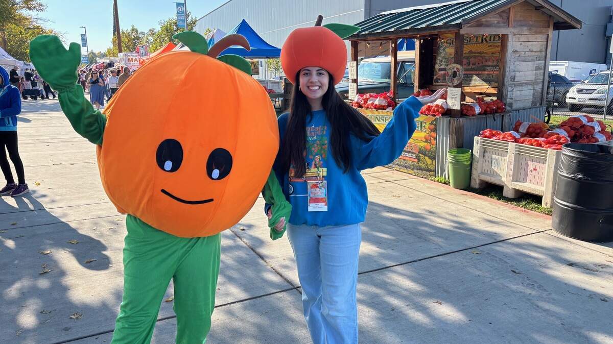Zippy the Mandarin, mascot for the 32nd annual Mountain Mandarin Festival, accompanied by Emily Garza, greets visitors to the festival in Roseville on Sunday, Nov. 23, 2025. The festival marks the beginning of the mandarin season in Placer County and draws thousands of visitors.