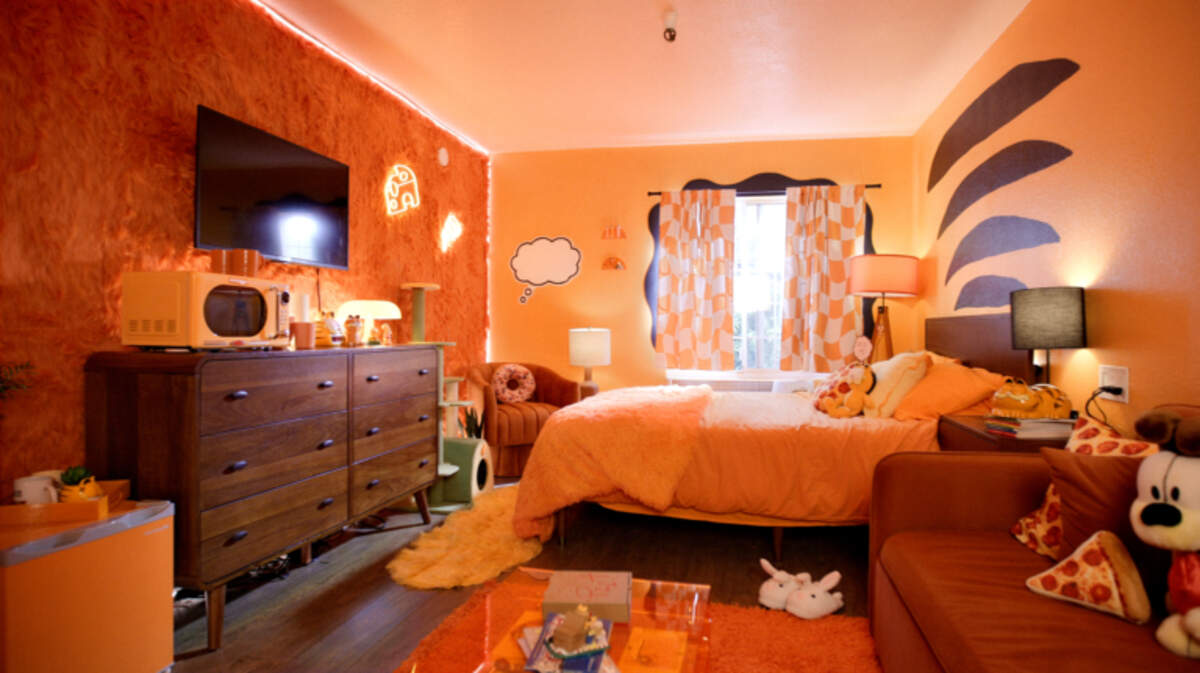 A Garfield-themed motel room at Motel 6 features orange fuzzy walls, neon signs and pizza-shaped throw pillows. “The Garfield Movie” is in theaters Friday, May 24, 2024.
