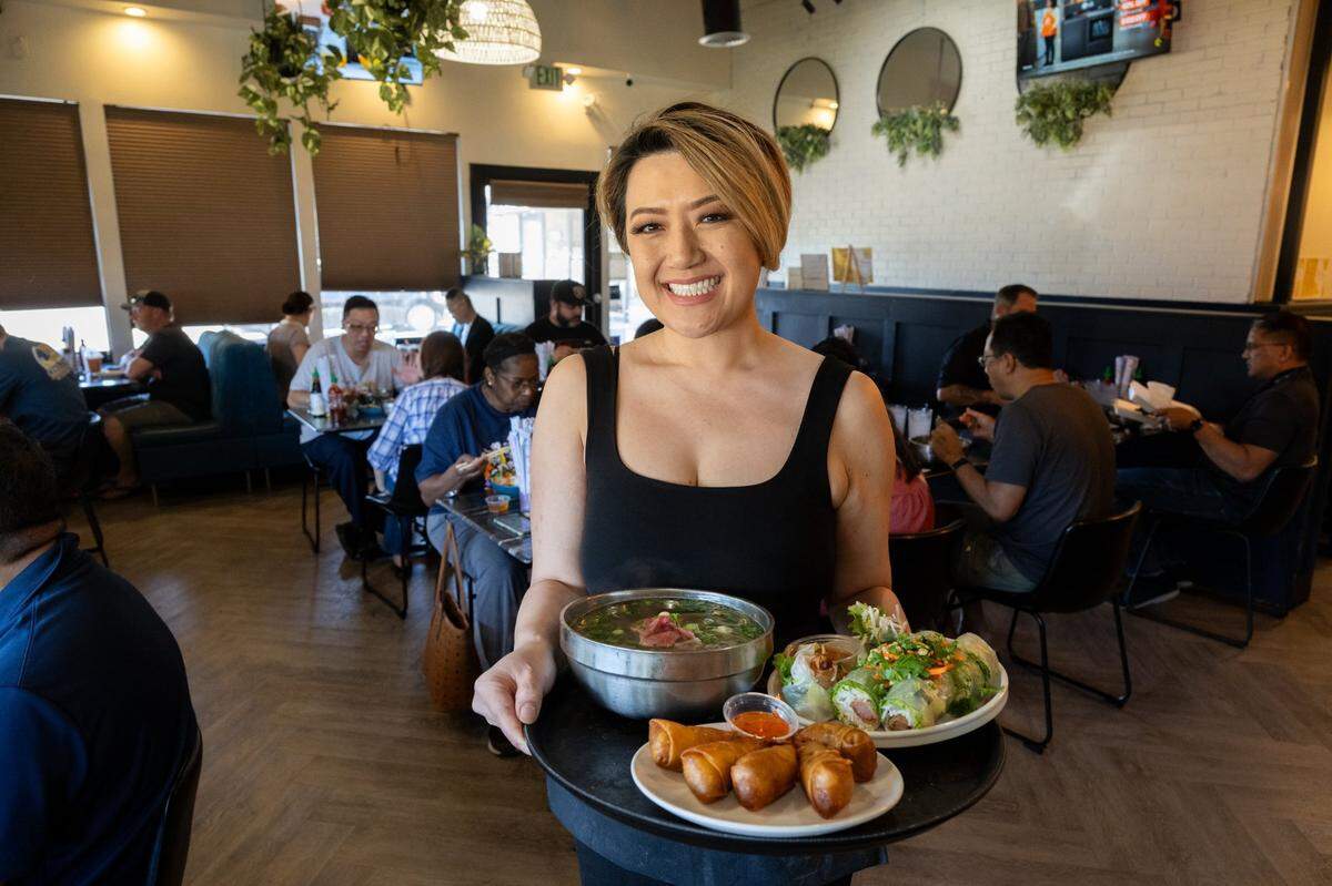 Owner My Le holds a tray of pho with brisket and lean beef, shrimp egg rolls and crispy sausage spring rolls at Pho Momma on Thursday, May 22, 2025, in La Riviera.