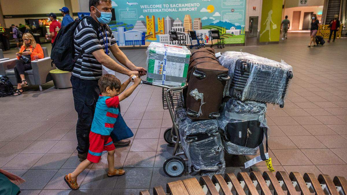 Afghan refugees Abdul, 46, and his youngest son Abdullah, 4, push a luggage cart belonging to their family of eight past a sign reading “Welcome to Sacramento International Airport” on Monday, Aug. 16, 2021. Their harrowing journey began the day before after the Taliban captured the city of Kabul, where Abdul had worked providing security to the U.S. embassy. “I thought our lives are in danger,” he said.