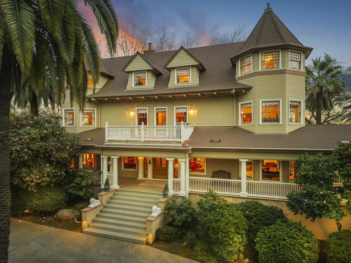 Hyholme’s hilltop facade, with its gables, turrets, and wrap‑around veranda, rises above mature trees on three landscaped acres overlooking Loomis.